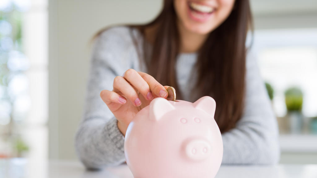 Junge Frau schmeißt lächelnd eine Münze in ein Sparschwein