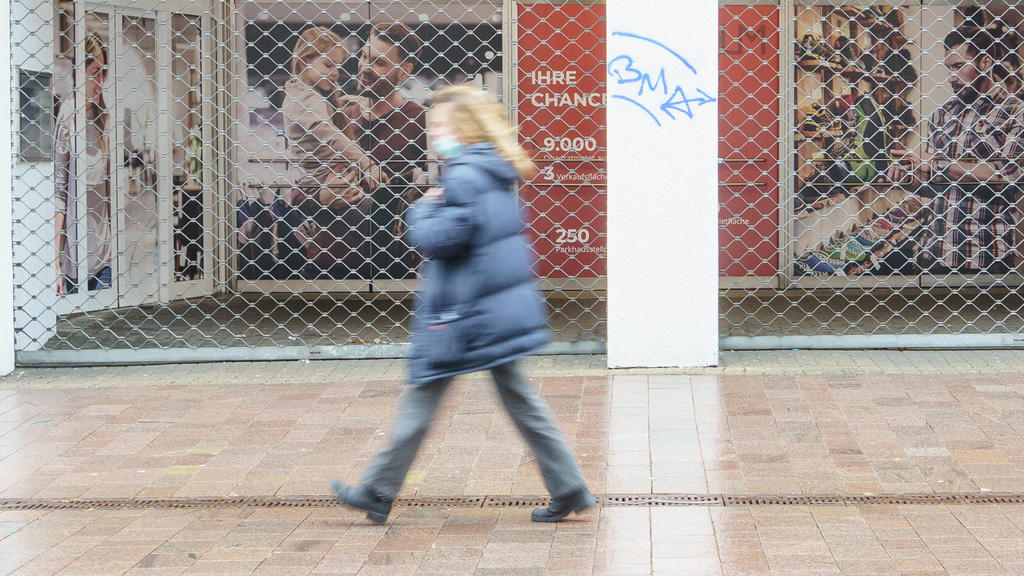 Die Flensburger Innenstadt ist im Zuge der Coronavirus-Pandemie zum Hochinzidenzgebiet erklärt worden, man sieht eine einzige Frau, wie sie mit Mund-Nasen-Schutz-Maske an einem geschlossenen Laden vorbeigeht.