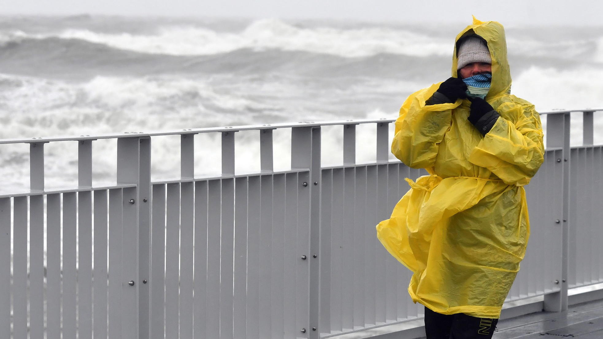 14.10.2020, Polen, Kolberg: Eine Frau, bekleidet mit einem Regenschutz, geht auf einem Steg an der stürmischen Ostsee entlang. Foto: Marcin Bielecki/PAP/dpa +++ dpa-Bildfunk +++