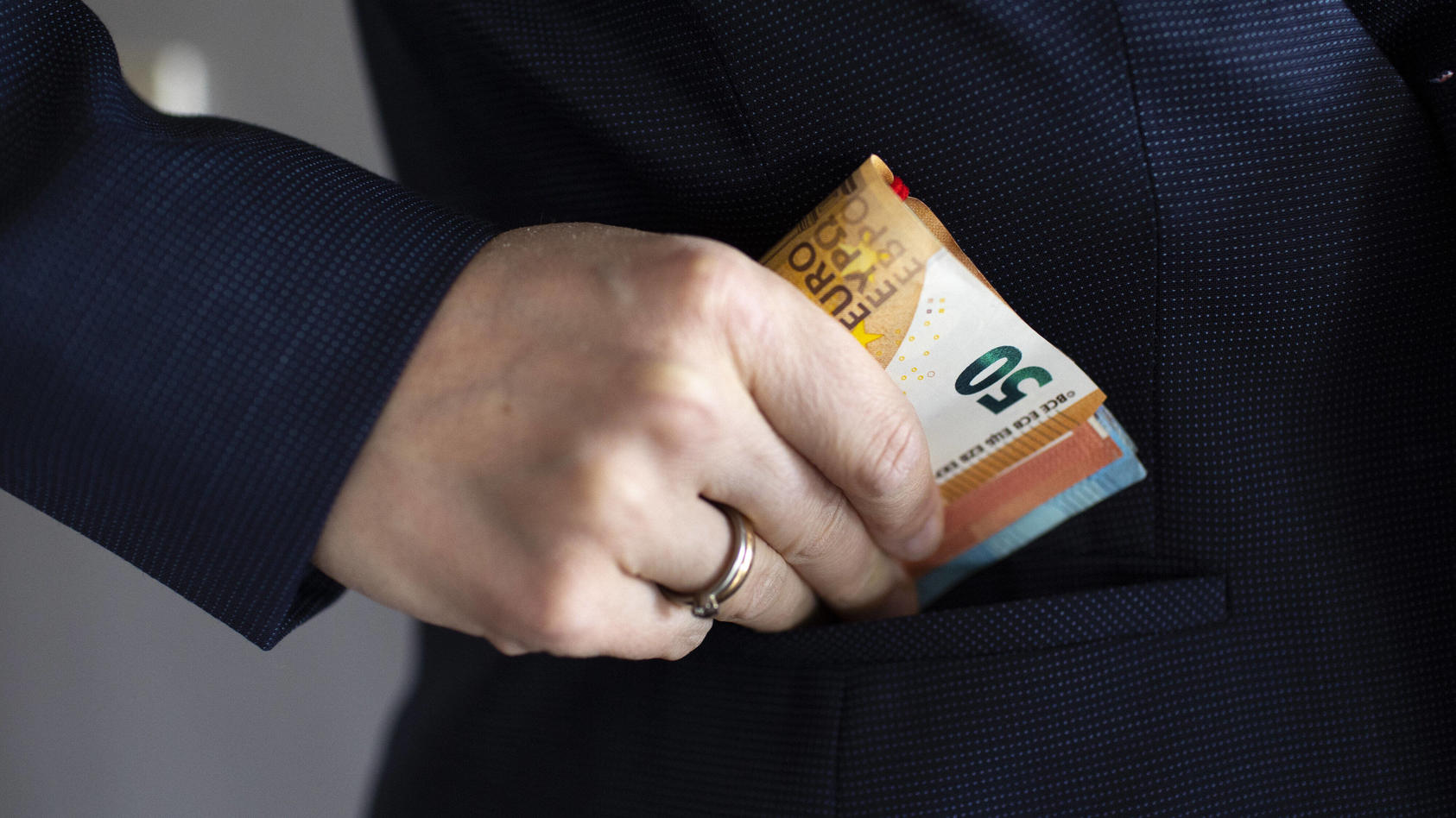 Eine Hand mit einem Ring steckt sich einen Stapel Euroscheine in die Jackentasche