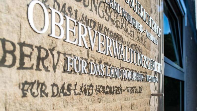 An der Aussenfassade am OVG hängt eine Hinweistafel mit dem Landeswappen von NRW und Schriftzügen. Foto: Guido Kirchner/dpa/Archivbild