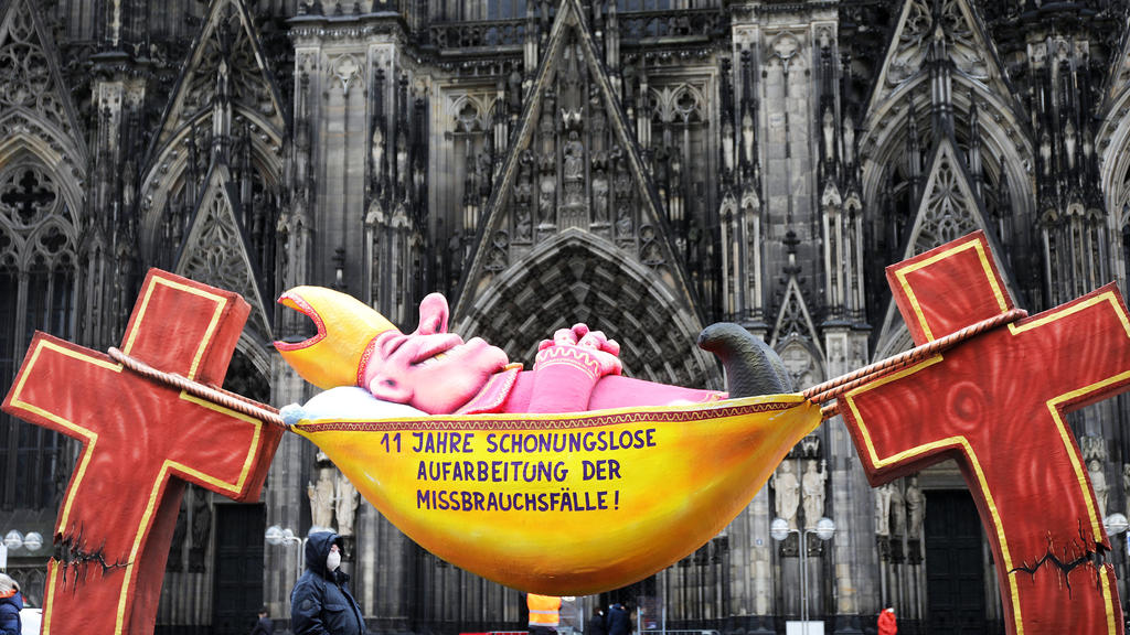 17.03.2021, Nordrhein-Westfalen, Köln: Die Plastik des Künstlers Jacques Tilly mit dem Slogan «11 Jahre schonungslose Aufarbeitung der Missbrauchsfälle!» steht vor dem Kölner Dom. Verschiedene Initiativen, die sich mit der Aufarbeitung des sexuellen