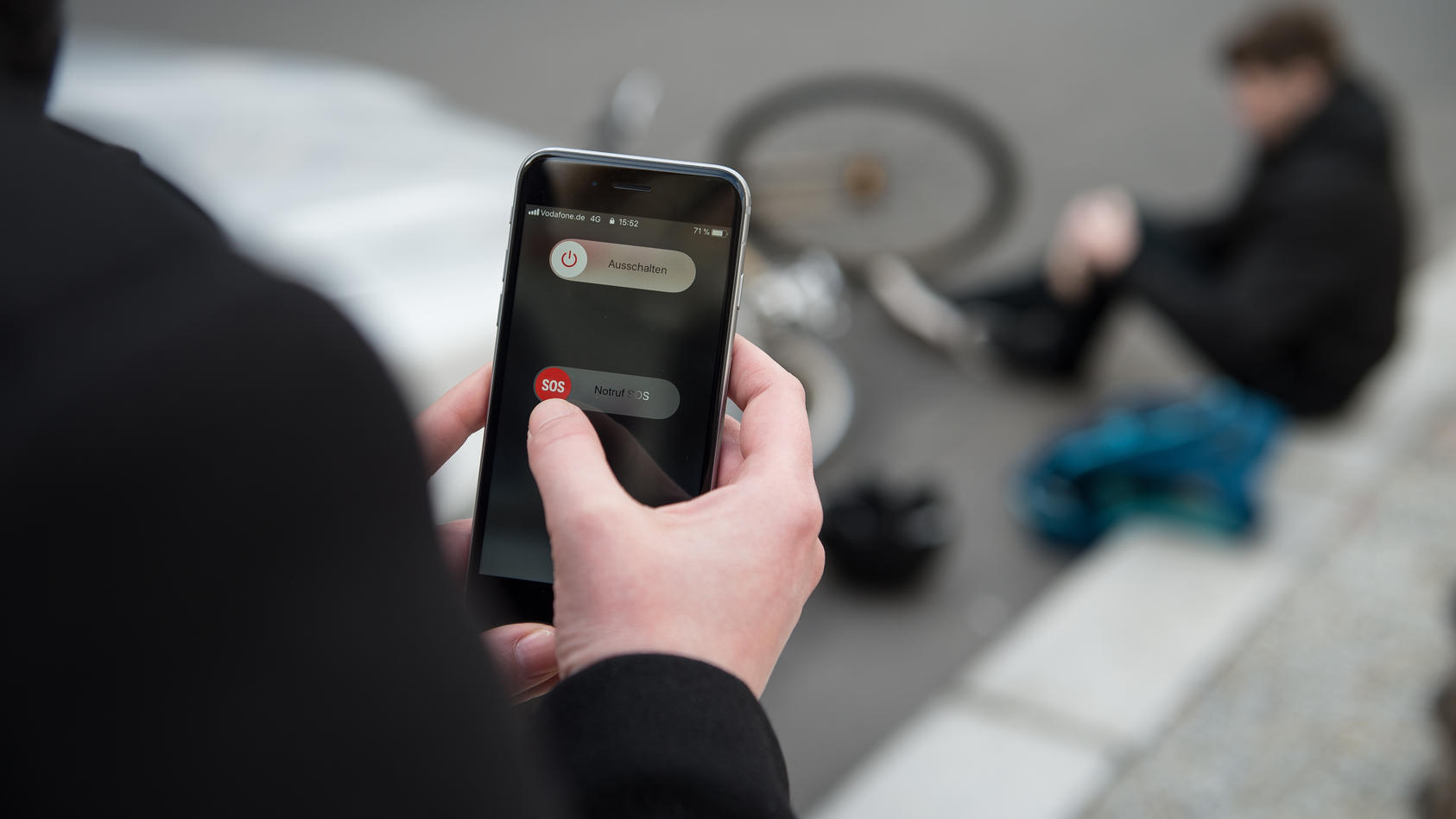 Eine Frau setzt einen Notruf mit einem Smartphone ab, nachdem ein Mann einen Fahrradunfall hatte. (Szene gestellt)