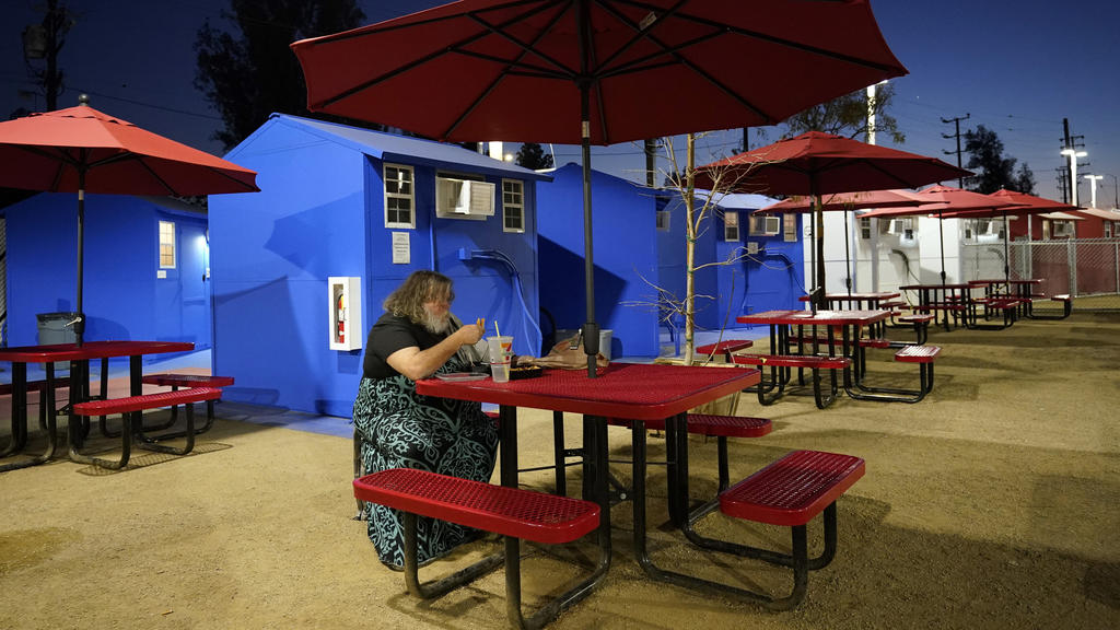 A resident eats in front of a row of tiny homes for the homeless, Thursday, Feb. 25, 2021, in the North Hollywood section of Los Angeles. (AP Photo/Marcio Jose Sanchez)