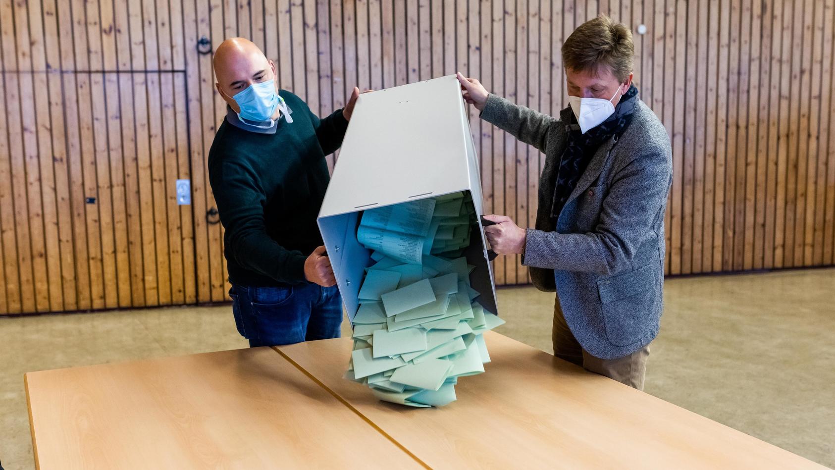 Wahlhelfer schütten eine Urne mit Stimmzetteln auf einem Tisch zur Auszählung aus.