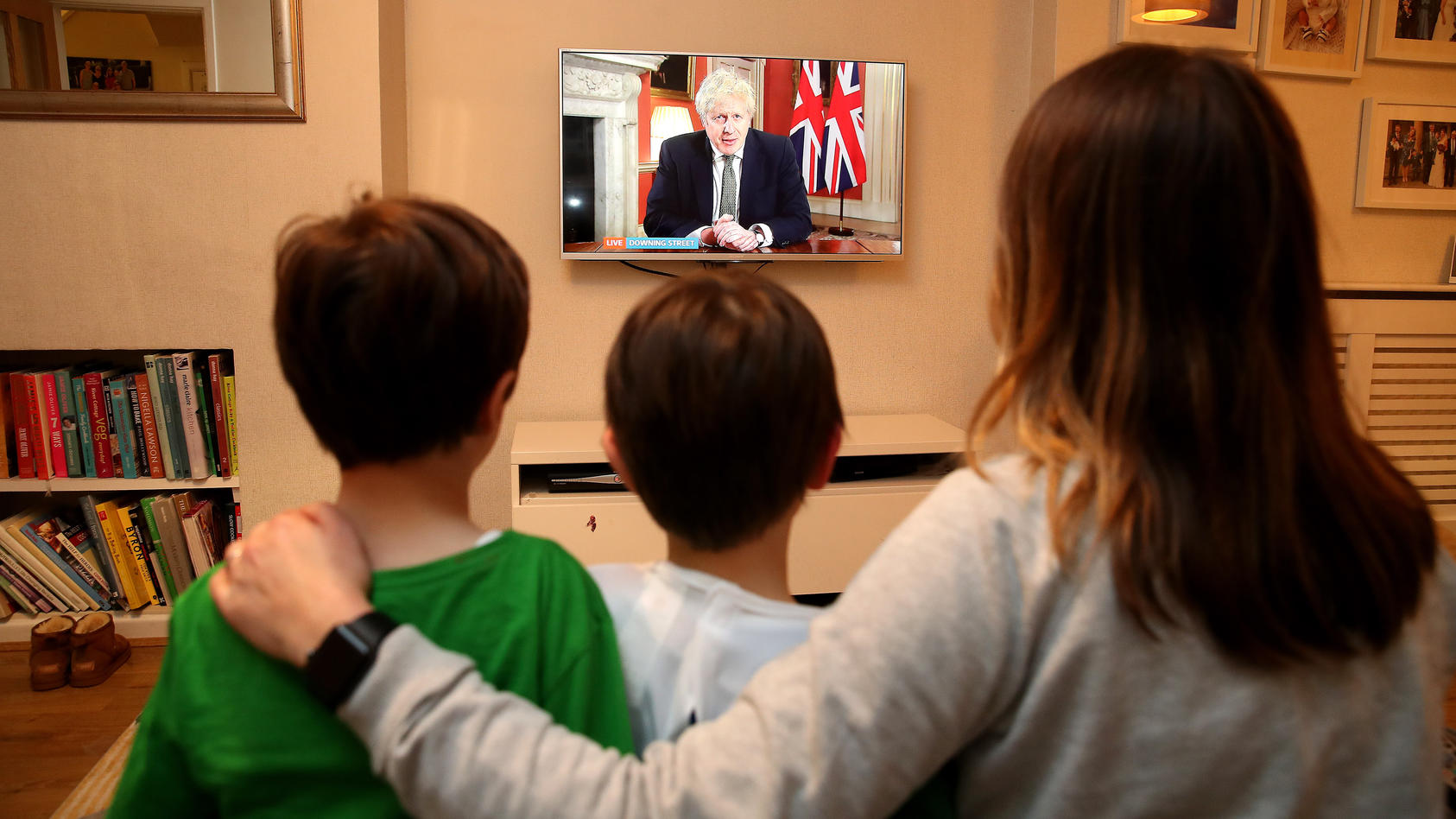 Eine britische Familie sitzt auf dem Sofa und schaut sich eine Nachrichtenübertragung mit Premierminister Boris Johnson im Fernsehen an.