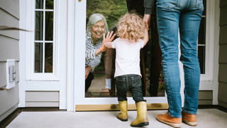 Mädchen begrüßt während der Coronakrise ihre Oma hinter einer Glasscheibe.