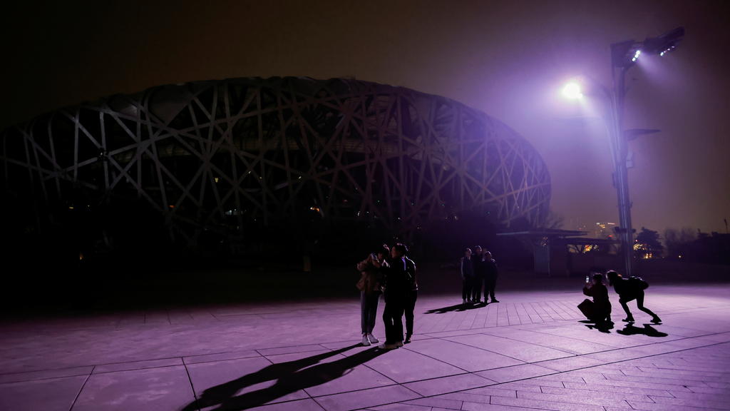 People stand in front of the National Stadium, also known as Birds' Nest, after the lights are turned off for Earth Hour in Beijing, China March 27, 2021. REUTERS/Thomas Peter