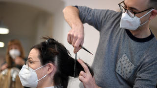 08.02.2021, Österreich, Wien: Ein Friseur schneidet einer Kundin in seinem Salon die Haare; beide tragen FFP2-Masken. Nach sechs Wochen Lockdown aufgrund der Corona-Pandemie öffnen in Österreich ab 08.02.2021 die Geschäfte wieder. Für körpernahe Dienstleistungen - wie zum Beispiel einen Friseur-Besuch - ist ein negativer Corona-Test nötig. Das Tragen einer besonders schützenden FFP2-Maske wird nahezu überall Pflicht. Foto: Roland Schlager/APA/dpa +++ dpa-Bildfunk +++