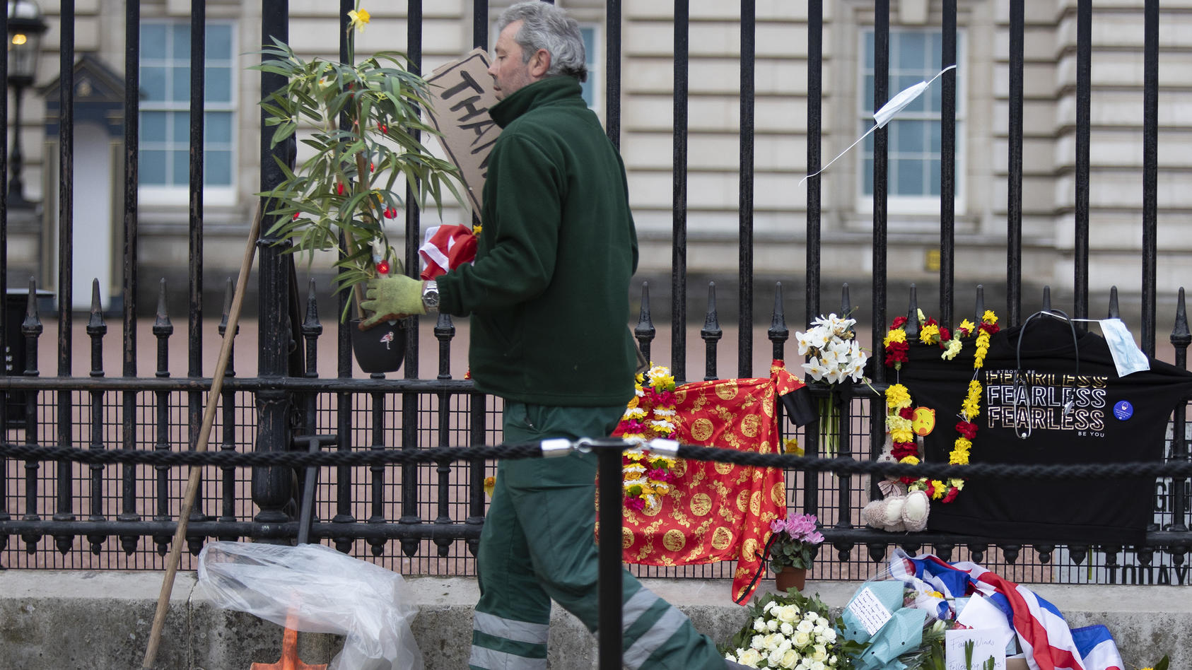 Ein royaler Mitarbeiter räumt die Blumen weg, die Trauernde für Prinz Philip vor dem Buckingham Palace niedergelegt haben.