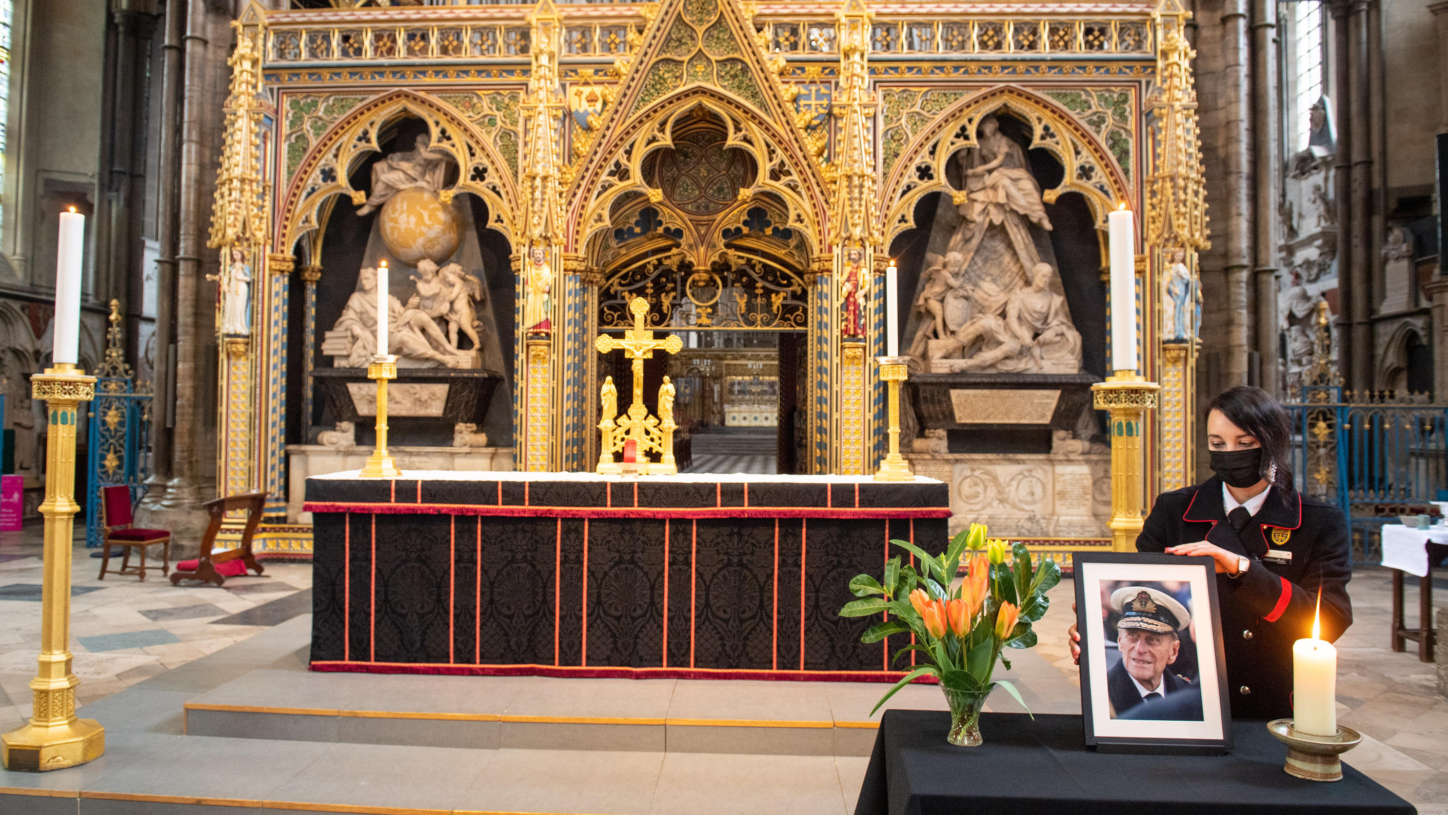 10.04.2021, Großbritannien, London: Rosa Wlodarczyk mit Mund-Nasen-Bedeckung justiert ein Foto des britischen Prinz Philip, Herzog von Edinburgh, das in der Westminster Abbey steht. Der Mann von Queen Elizabeth II. war am 09.04.2021 im Alter von 99 J
