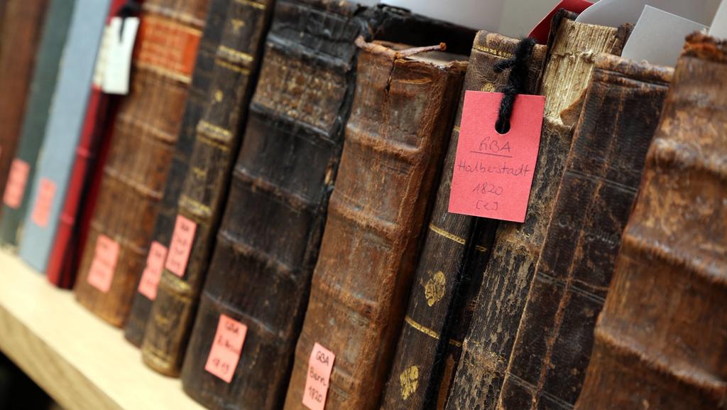 In einem Regal, vermutlich in einer Bibliothek, stehen nebeneinander gereiht einige sehr alte Bücher.