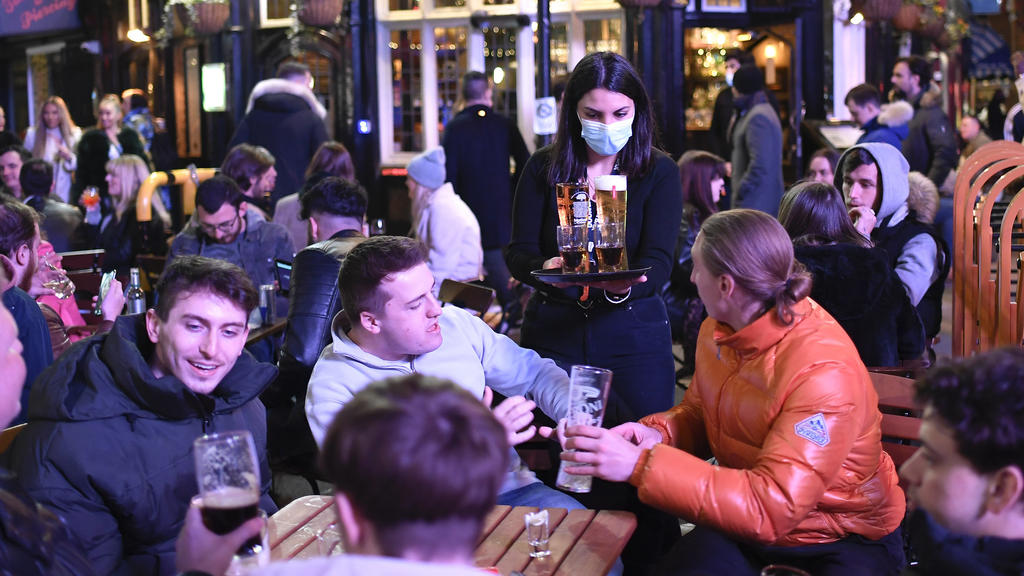 A waitress serves drinks as customers sit at setup tables outside pubs in Soho, in London, on the day some of England's third coronavirus lockdown restrictions were eased by the British government, Monday, April 12, 2021. People across England flocke