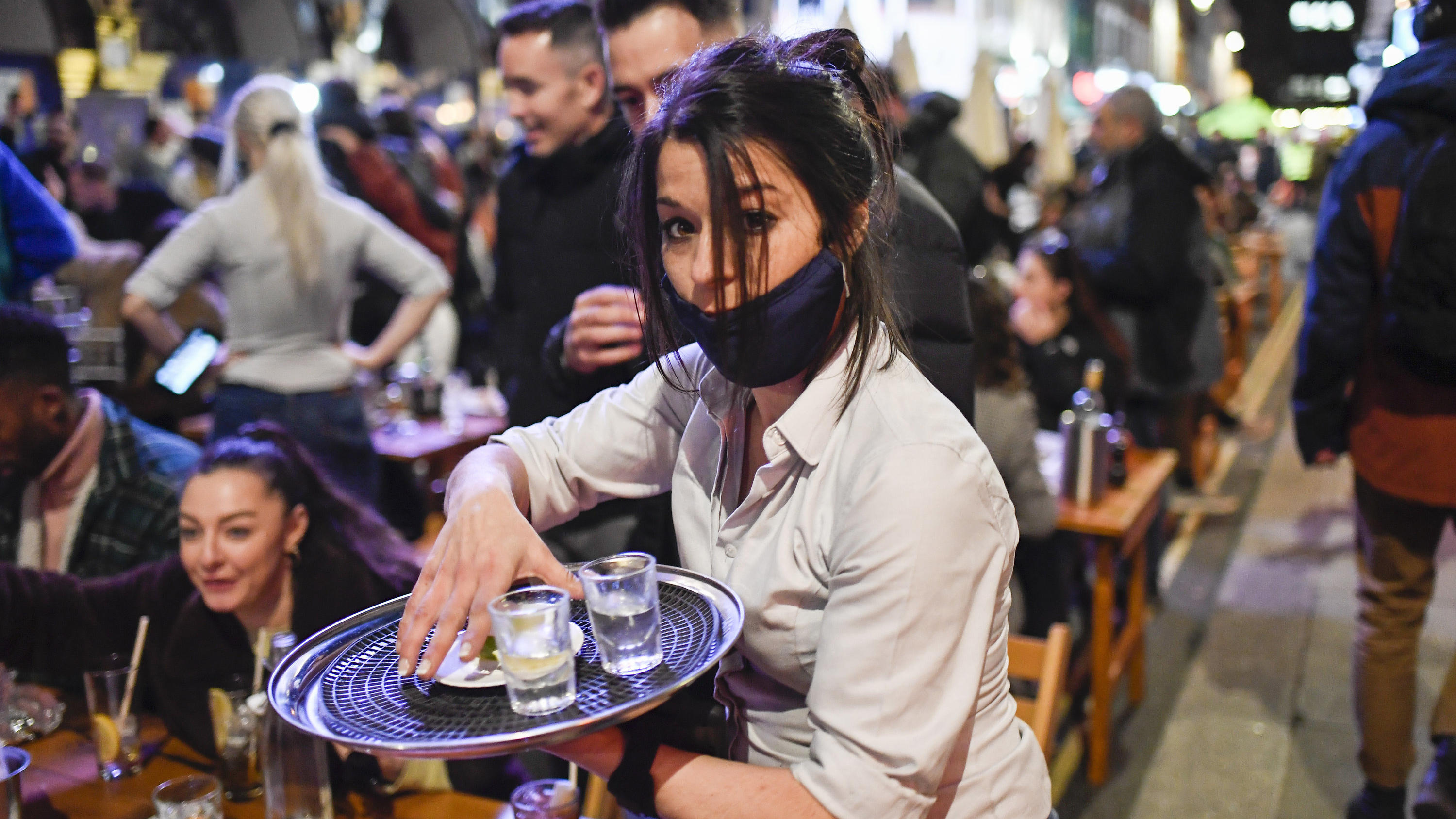 A waitress serves drinks at tables outside a pub in Soho, London, on the day some of England's coronavirus lockdown restrictions were eased by the British government, Monday, April 12, 2021. Pubs, shops and hairdressers have opened as lockdown restri