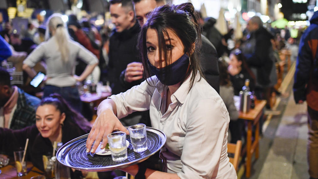 A waitress serves drinks at tables outside a pub in Soho, London, on the day some of England's coronavirus lockdown restrictions were eased by the British government, Monday, April 12, 2021. Pubs, shops and hairdressers have opened as lockdown restri
