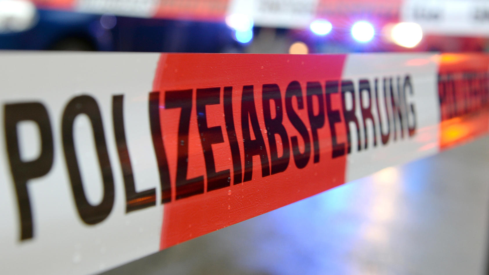 ARCHIV - ILLUSTRATION - Ein Flatterband mit der Aufschrift «Polizeiabsperrung» ist am 05.11.2014 in Freiburg (Baden-Württemberg) an einem Einsatzort vor einem Feuerwehrfahrzeug mit Blaulicht zu sehen. Mit einem Samuraischwert soll ein 38-Jähriger sei
