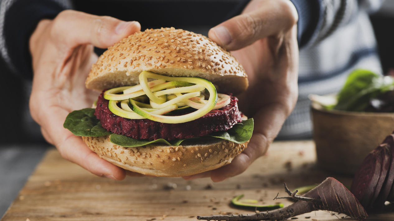 Ein junger Mann hält einen appetitlichen Veggie-Burger in der Hand