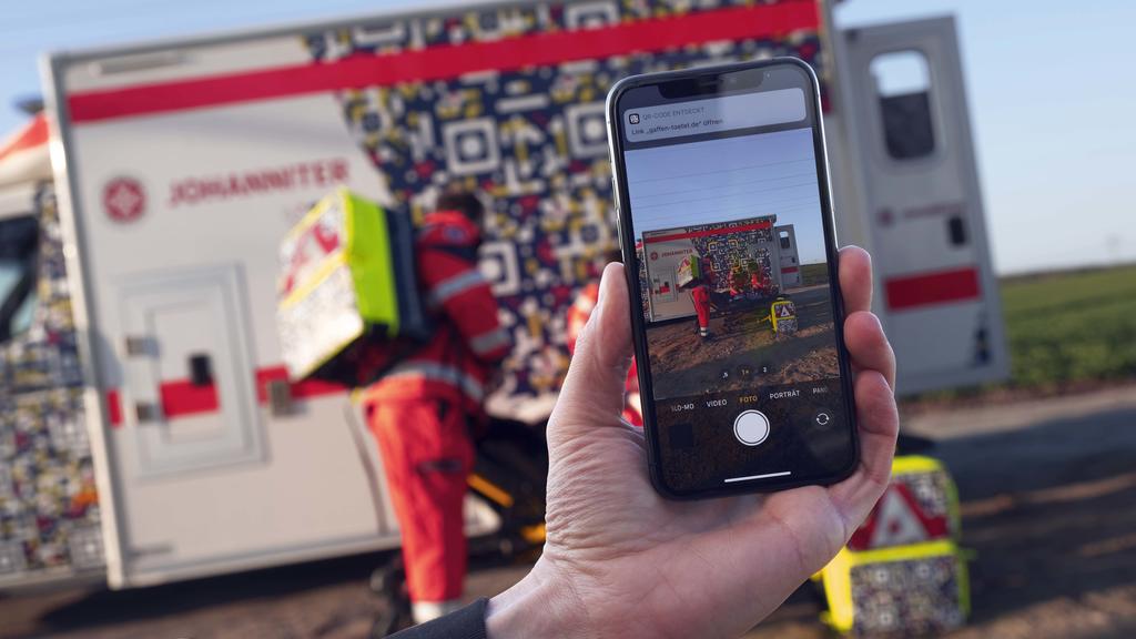 In einer gestellten Szene der Johanniter-Unfall-Hilfe ist auf einem Smartphone der QR-Code auf einem Rettungswagen zu sehen, der die Botschaft "Gaffen tötet" enthält.