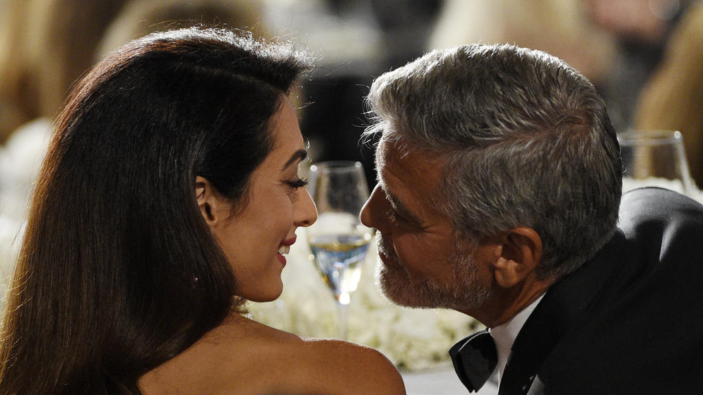 ARCHIV - 07.06.2018, USA, Los Angeles: George Clooney, Schauspieler aus den USA, und seine Frau Amal, Menschenrechtsanwältin aus dem Libanon, sprechen miteinander bei der Verleihung des AFI-Preises für Clooneys Lebenswerk. Er führt Regie, steht vor d