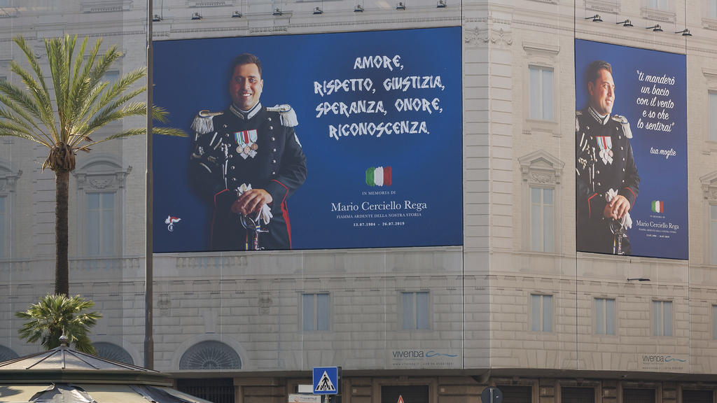 Plakate an dem Platz, auf dem Mario Cerciello Rega erstochen wurde. Auf dem linken steht auf Italienisch: "Liebe, Respekt, Gerechtigkeit, Hoffnung, Ehre , Dankbarkeit ", links," Ich werde dir einen Kuss in den Wind blasen und ich weiß, dass du es füh