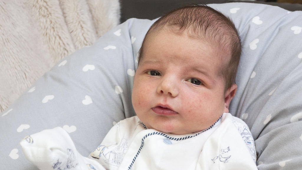 Baby Jorge liegt auf einem Kissen und schaut in die Kamera.