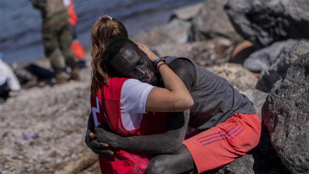 18.05.2021, Spanien, Ceuta: Ein Mitglied des Spanischen Roten Kreuzes tröstet einen Migranten, und umarmt ihn am Strand in der spanischen Enklave Ceuta. Spanien soll bereits 2700 der gut 6000 vom Gebiet Marokkos aus in Ceuta eingedrungenen Menschen w