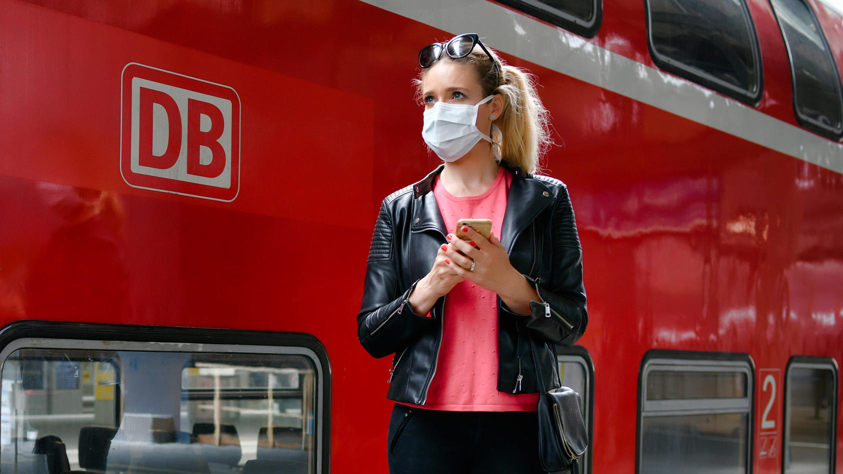 Frau mit Mundschutzmaske, wartet auf Zug.
