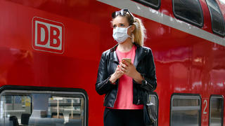 Frau mit Mundschutzmaske, wartet auf Zug