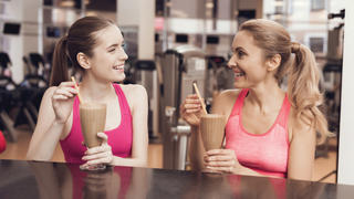 Eine Mutter und ihre Tochter trinken nach dem Training im Fitnessstudio einen Protein-Shake an der Bar.
