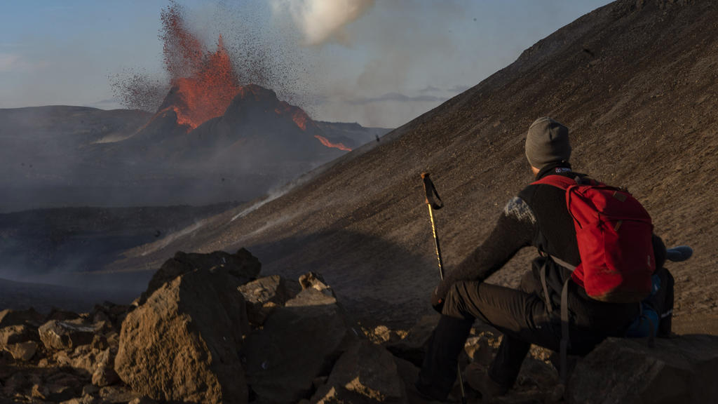 A man watches as lava spews from an eruption of the Fagradalsfjall volcano on the Reykjanes Peninsula in southwestern Iceland on Tuesday, May 11, 2021. (AP Photo/Miguel Morenatti)