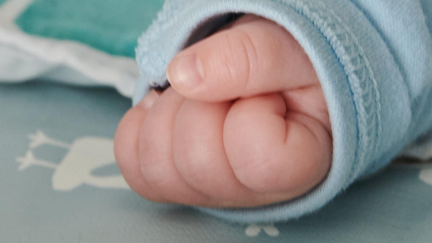 Bei einem Hausbesuch einer Hebamme ist die Hand des nur wenige Wochen alten Babys ist zu einer kleinen Faust geballt, während es auf dem Wickeltisch liegt. Am 10.05.2021 werden die beliebtesten Vornamen 2020 bekanntgegebe