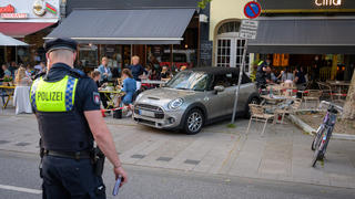 02.06.2021, Hamburg: Ein Polizist steht vor dem Unfallauto, das zwischen Fahrrädern, Tischen, Stühlen und zerstörtem Geschirr steht. Ein Mann ist mit einem Leihauto rückwärts in den Außenbereich eines Restaurants in Hamburg gefahren. Vier Menschen seien leicht verletzt worden, sagte ein Polizeisprecher. Foto: Jonas Walzberg/dpa - ACHTUNG: Autokennzeichen und Privatpersonen gepixelt +++ dpa-Bildfunk +++