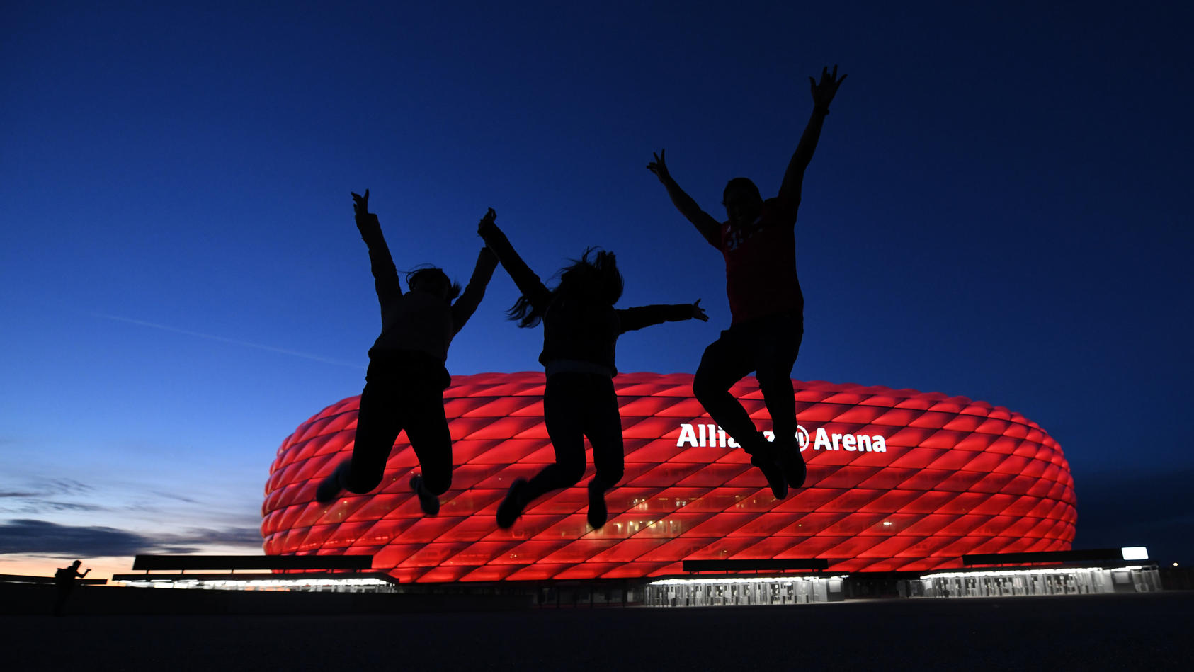 08.05.2021, Bayern, München: Drei Fans springen nach der Partie in der Fußball Bundesliga FC Bayern München - Borussia Mönchengladbach vor der Allianz Arena in die Höhe. Einige Fans haben sich vor dem Stadion versammelt. Die neuen Corona-Bestimmungen