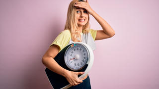 Eine junge, blonde Frau hält eine Waage unter ihrem Arm.