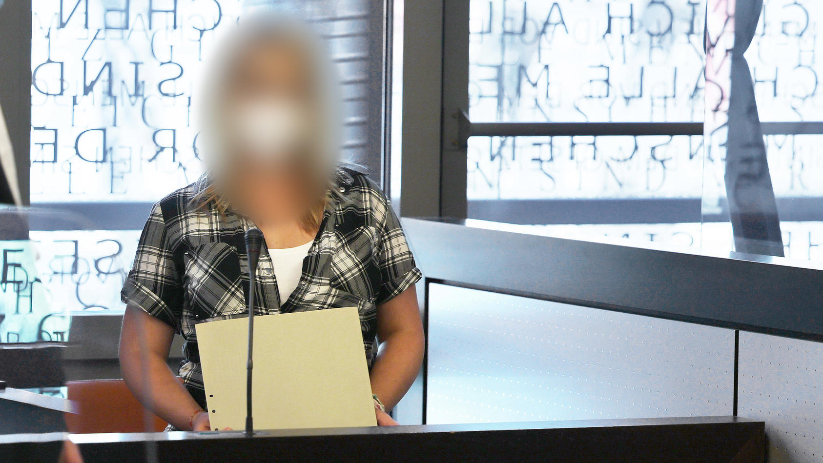Die angeklagte Mutter (r) spricht mit einem ihrer Anwälte - in einer wegen Corona angebrachten Scheibe spiegelt sich das Wort "Gesetz" vom Fenster.