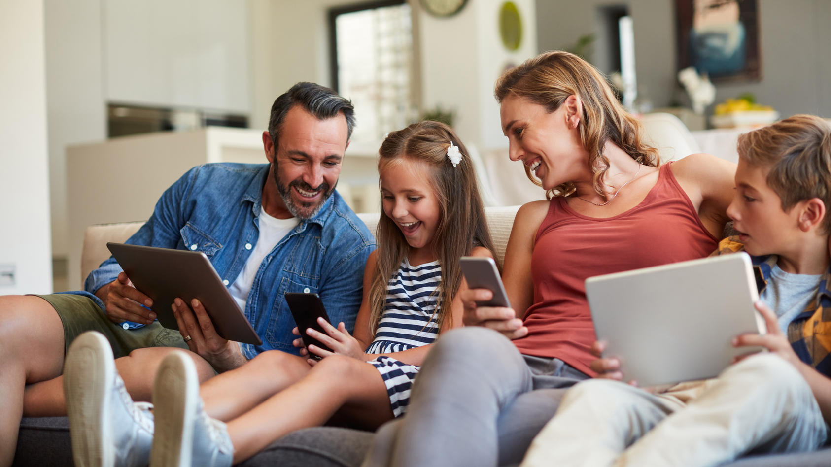 Eine glückliche Familie nutzt mobile Geräte auf dem Sofa.
