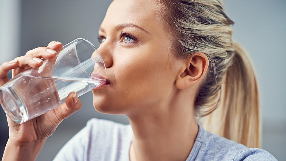 Eine junge Frau trinkt stilles Wasser aus einem Glas.