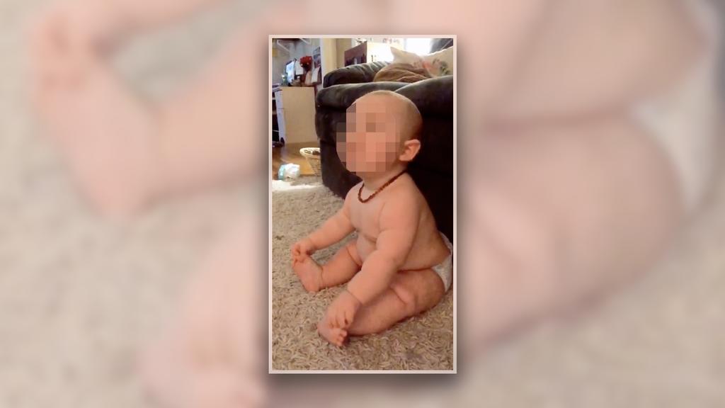 Dickes Baby sitzt in Windeln auf einem Teppich