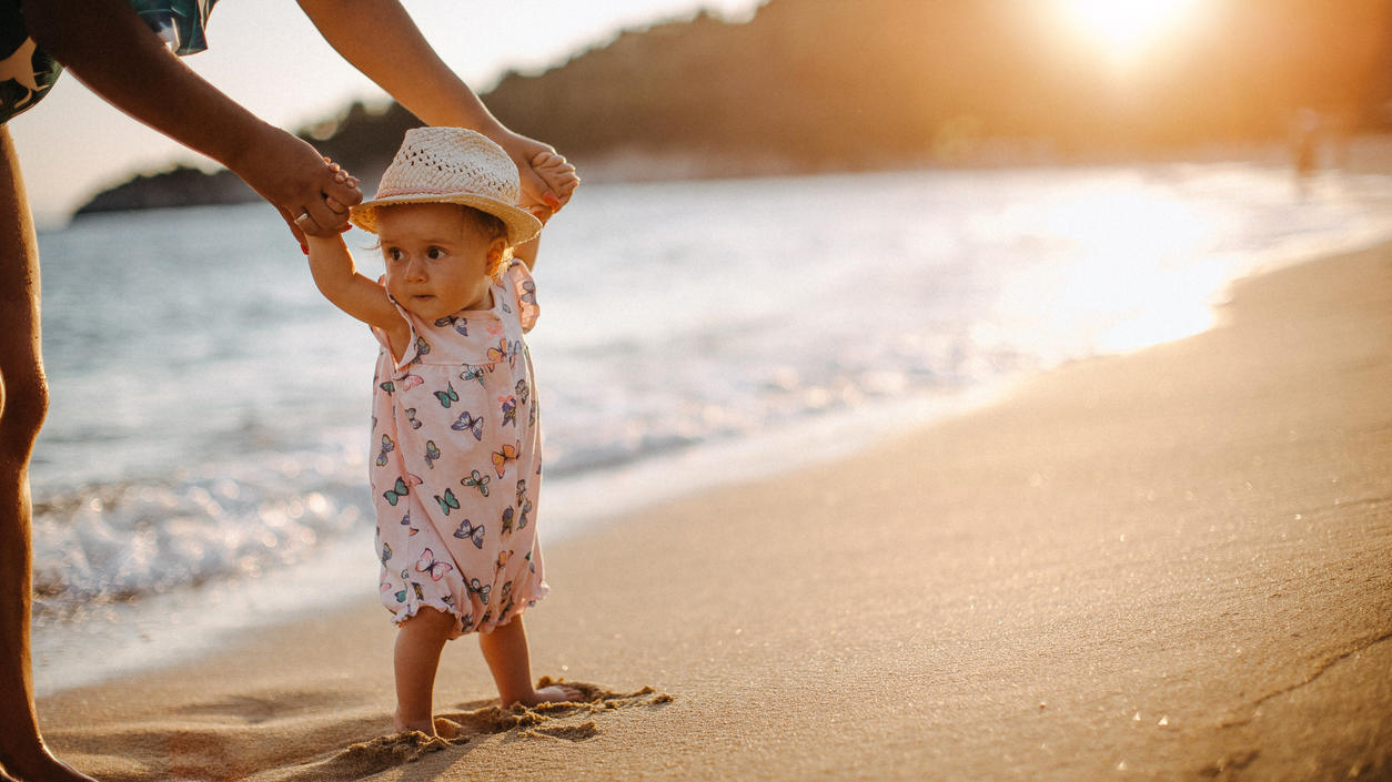 Kleinkind läuft an den Händen der Mutter am Strand