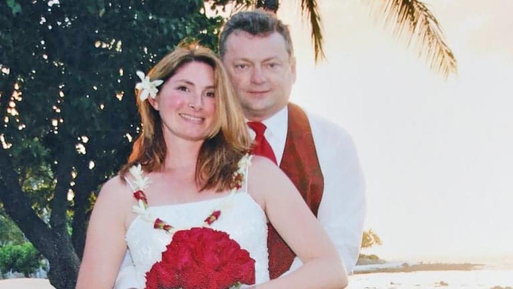 Eine junge blonde Frau wird im Hochzeitskleid von ihrem Bräutigam gehalten.