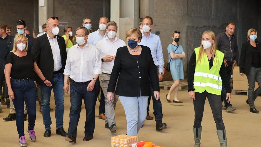 20.07.2021, Nordrhein-Westfalen, Bad Münstereifel: Bundeskanzlerin Angela Merkel (CDU, M)und der Ministerpräsident von Nordrhein-Westfalen Armin Laschet (CDU, 3.v.l) besichtigen ein Lager mit Lebensmitteln bei ihrem Besuch im vom Hochwasser betroffen
