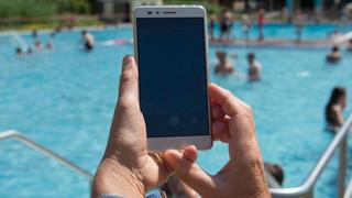 Eine Frau hält im Freibad ein Smartphone in Richtung des Pools