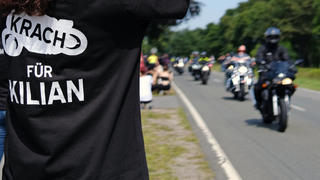 24.07.2021, Niedersachsen, Rhauderfehn: Eine Frau mit einem T-Shirt mit der Aufschrift "Krach für Kilian" winkt den Motorradfahrern, die am Haus des krebskranken Kilian vorbei fahren. Mehrere Tausend Motorradfahrer und -fahrerinnen haben sich getroffen, um dem kranken Jungen eine Freude zu machen. Das Kind ist großer Motorradfan. Foto: Markus Hibbeler/dpa +++ dpa-Bildfunk +++