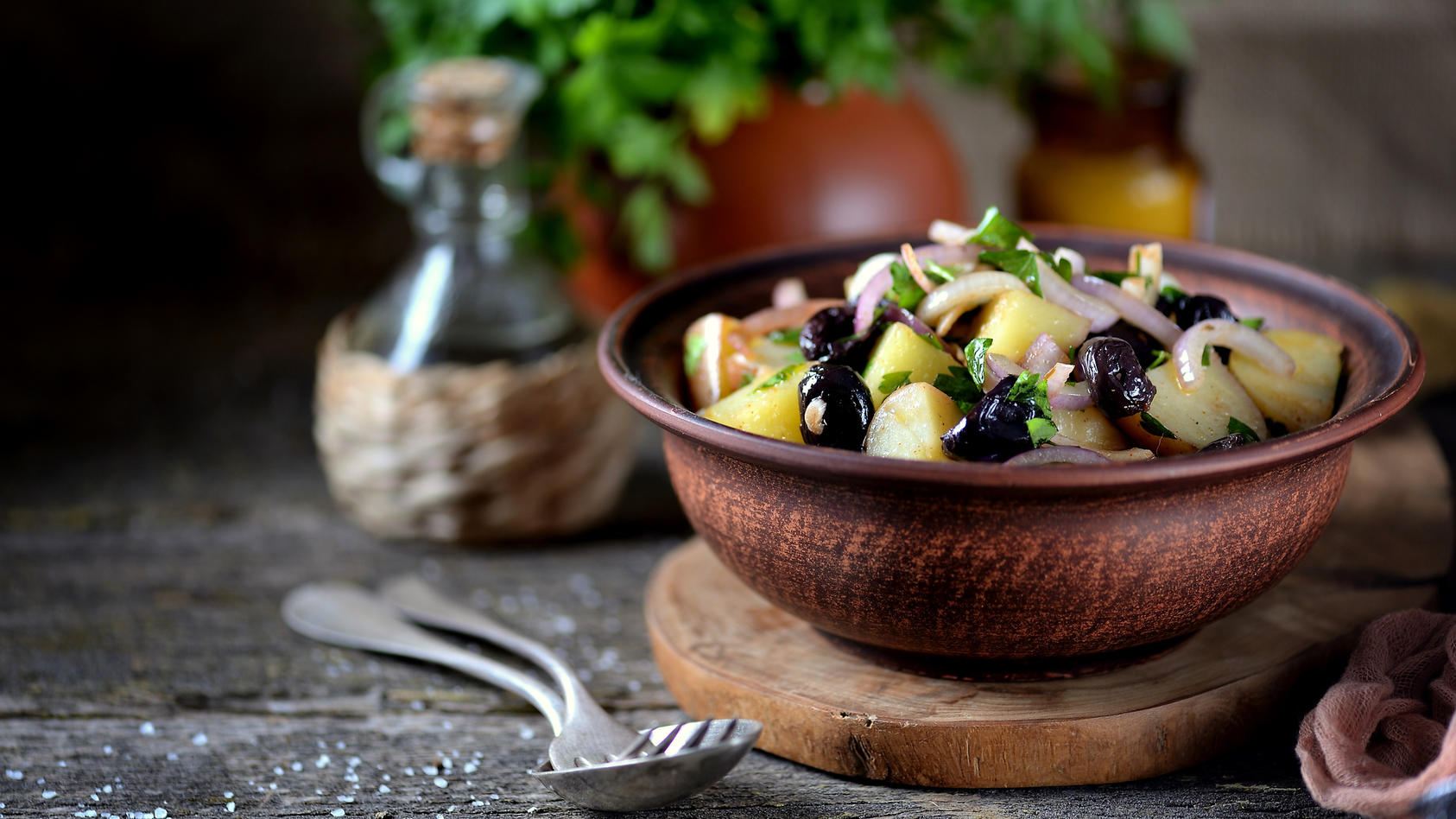 Kartoffelsalat mit Oliven und Zwiebeln in einer braunen Schüssel angerichtet