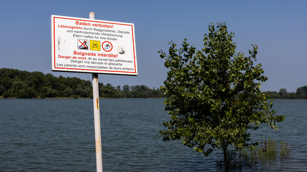 20.07.2021, Baden-Württemberg, Neuried: Ein Schild mit Aufschrift «Baden verboten! - Lebensgefahr» steht am Ufer eines Überflutungsgebietes in der Nähe des Rheins während im Hintergrund ein Baum im Wasser steht. Angesichts der Hochwasser-Katastrophe