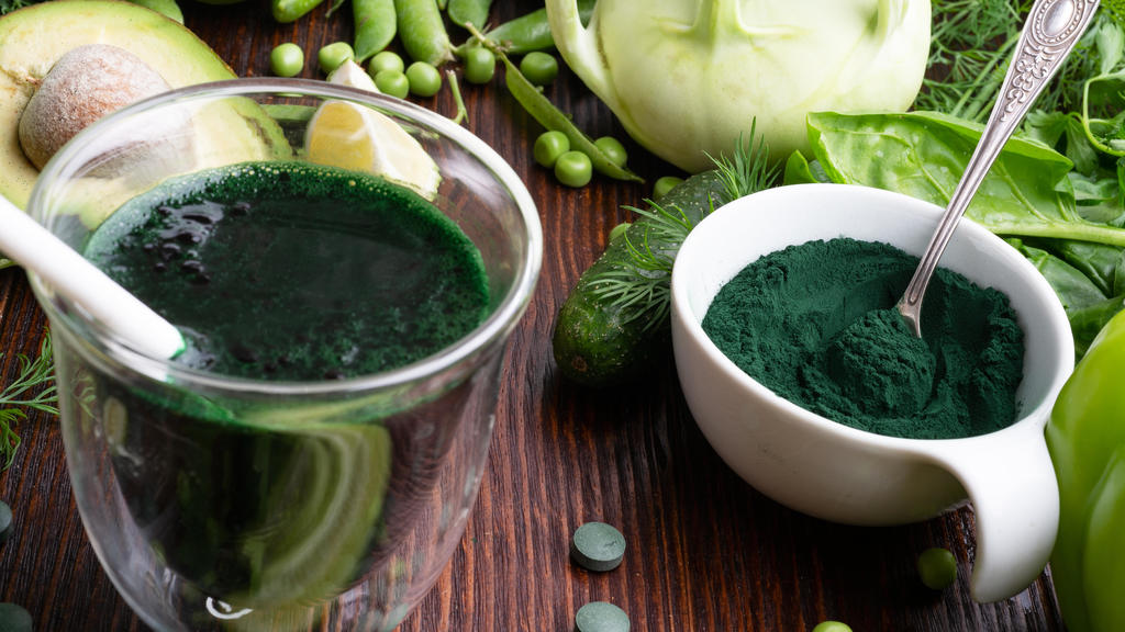 Spirulina-Pulver und -Smoothie vor grünem Gemüse