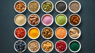 Verschiedene Superfoods in kleinen Gläsern, zum Beispiel Matcha, Spirulina, Quinoa, Goji-Beeren