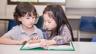 Zwei Kinder sitzen nebeneinander und schauen gemeinsam in ein Buch.