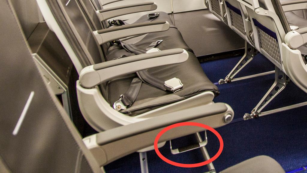 Eine leere Sitzreihe im Flugzeug. Rot umrandet ist ein kleiner Tritt am unteren Rand des Sitzgestells.