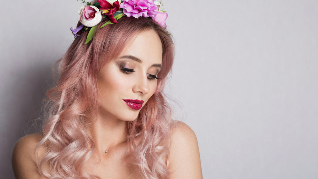Frau mi roséfarbenen Haaren und Blumenkranz im Haar.